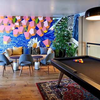 A room featuring a pool table, large wall mural and two upholstered chairs near a small round table