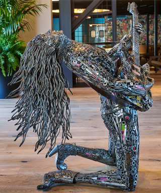 A woman made in metal sculpture with long hair, on her knees holding a guitar